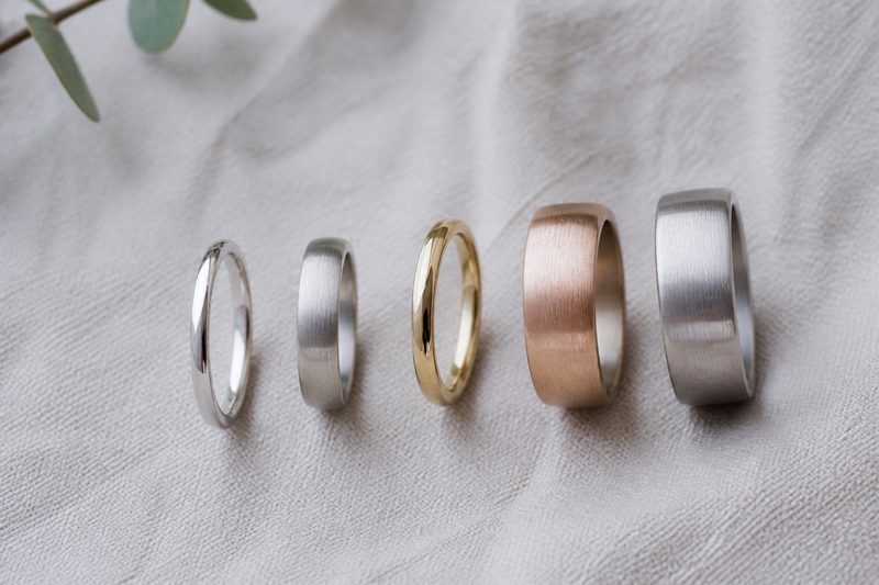 Five men's wedding bands arranged from narrowest to widest on linen