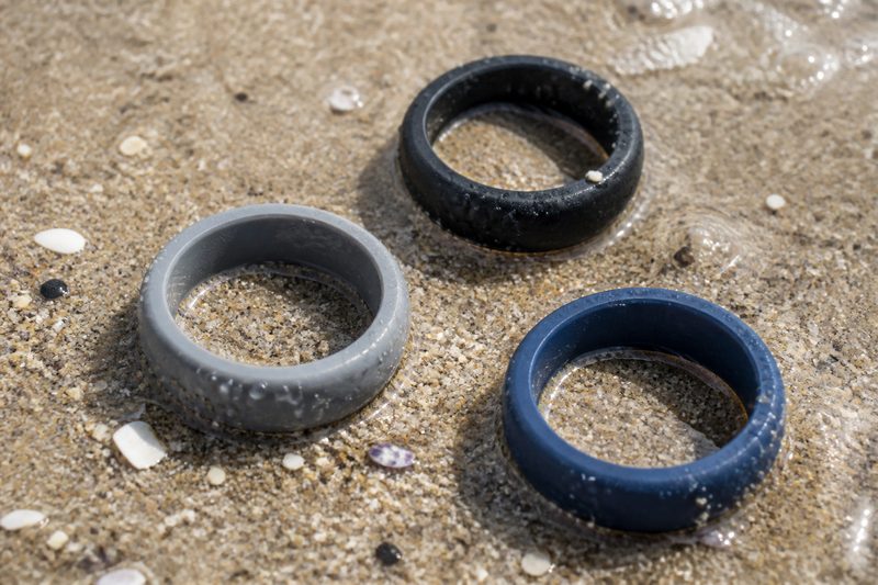 Three silicone wedding rings in black, grey and navy on wet beach sand