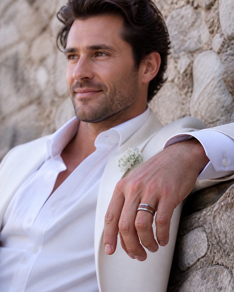Groom leaning on a rustic wall wearing a distinctive wood-inlay wedding band