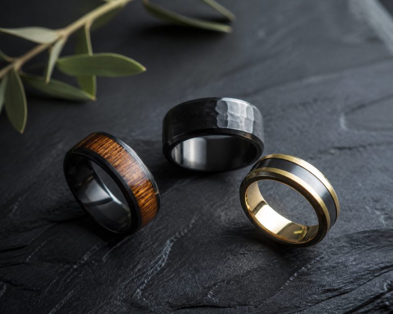 Three unconventional men's wedding rings including wood inlay and two-tone styles