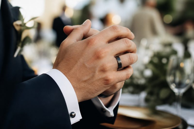 Groom's clasped hands at a wedding reception showing a dark metal wedding band